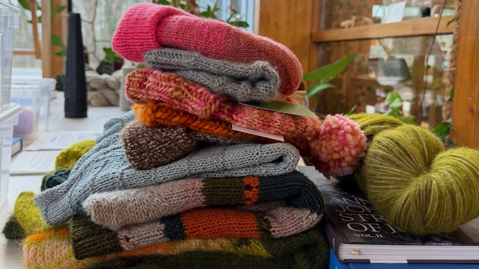 Close up van een stapel kleurrijke gebreide projecten, een handgeverfde streng Alpcac Air en 2 boeken