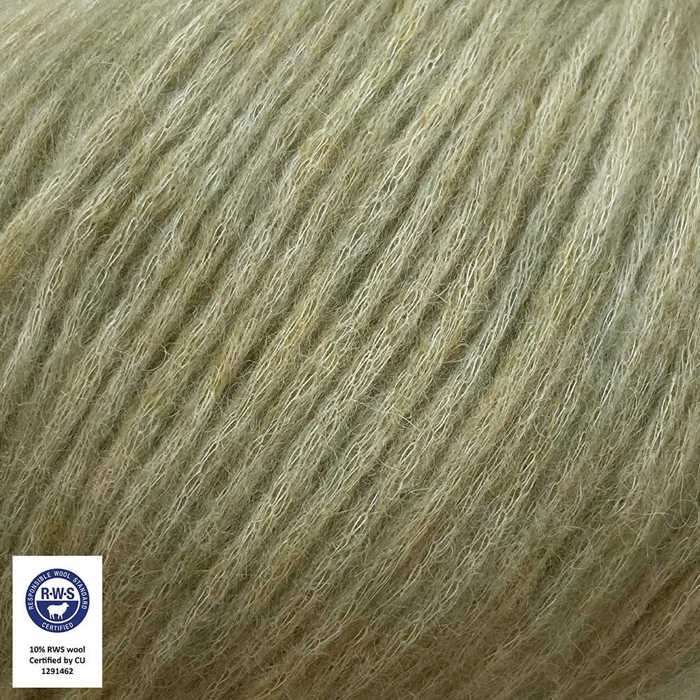 Close-up van een bol Snefnug-garen in een zachte, pistache kleur. Dit lichte blowyarn heeft een kern van katoen met ingeblazen alpaca- en merinovezels, wat zorgt voor een luchtige, pluizige structuur. Onderaan zijn de RAS- en RWS-certificeringslogo's zichtbaar.