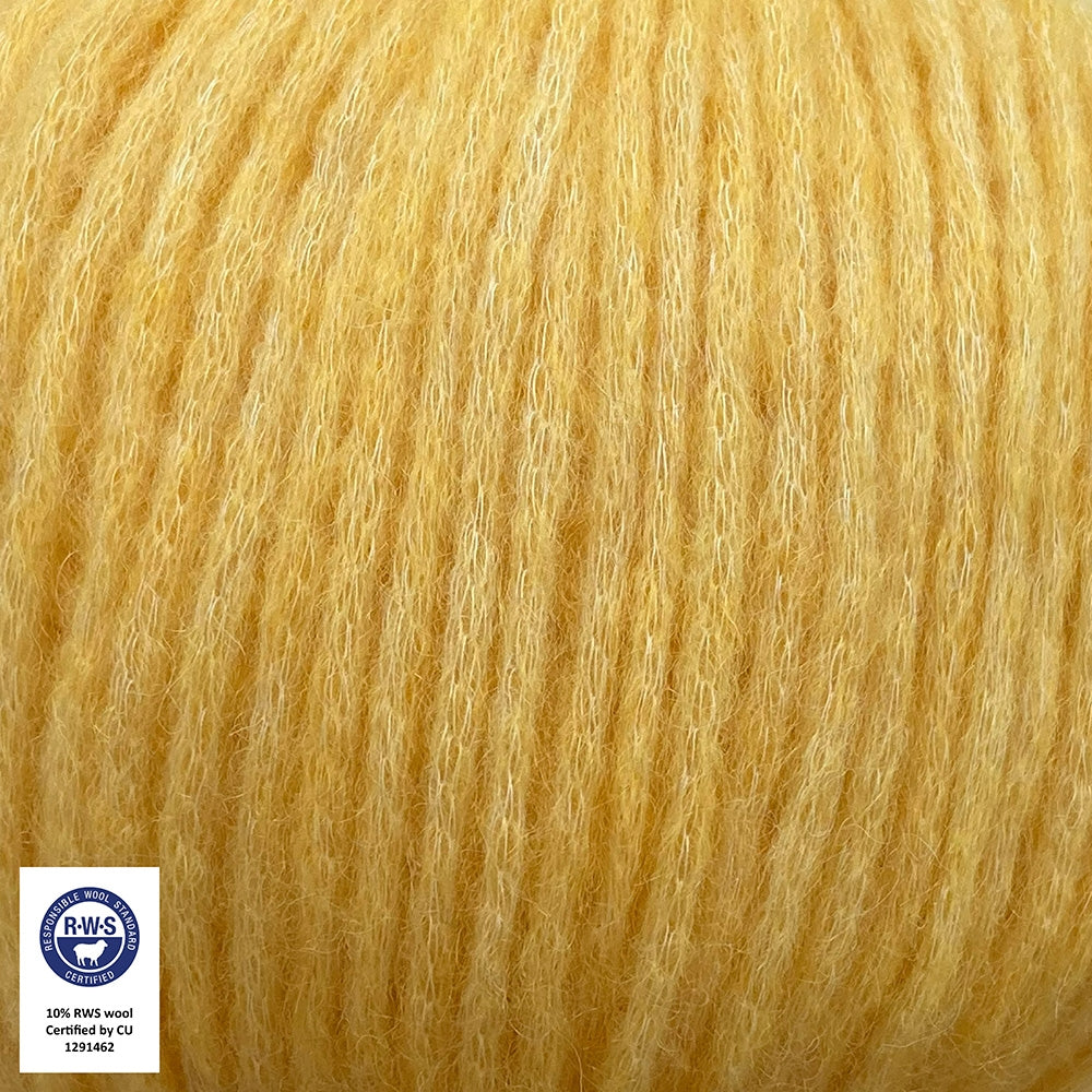Close-up van een bol Snefnug-garen in een banaangele kleur. Dit lichte blowyarn heeft een kern van katoen met ingeblazen alpaca- en merinovezels, wat zorgt voor een luchtige, pluizige structuur. Onderaan zijn de RAS- en RWS-certificeringslogo's zichtbaar.