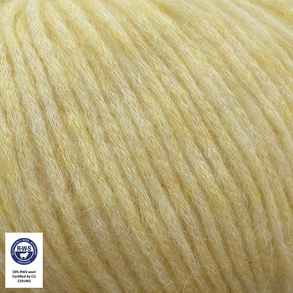 Close-up van een bol Snefnug-garen in een zachte, lichtgele kleur. Dit lichte blowyarn heeft een kern van katoen met ingeblazen alpaca- en merinovezels, wat zorgt voor een luchtige, pluizige structuur. Onderaan zijn de RAS- en RWS-certificeringslogo's zichtbaar.
