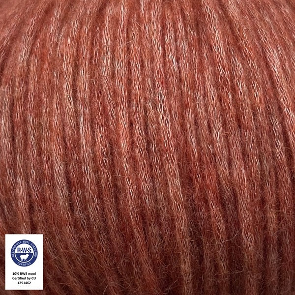 Close-up van een bol Snefnug-garen in een baksteen oranje/rode kleur. Dit lichte blowyarn heeft een kern van katoen met ingeblazen alpaca- en merinovezels, wat zorgt voor een luchtige, pluizige structuur. Onderaan zijn de RAS- en RWS-certificeringslogo's zichtbaar.