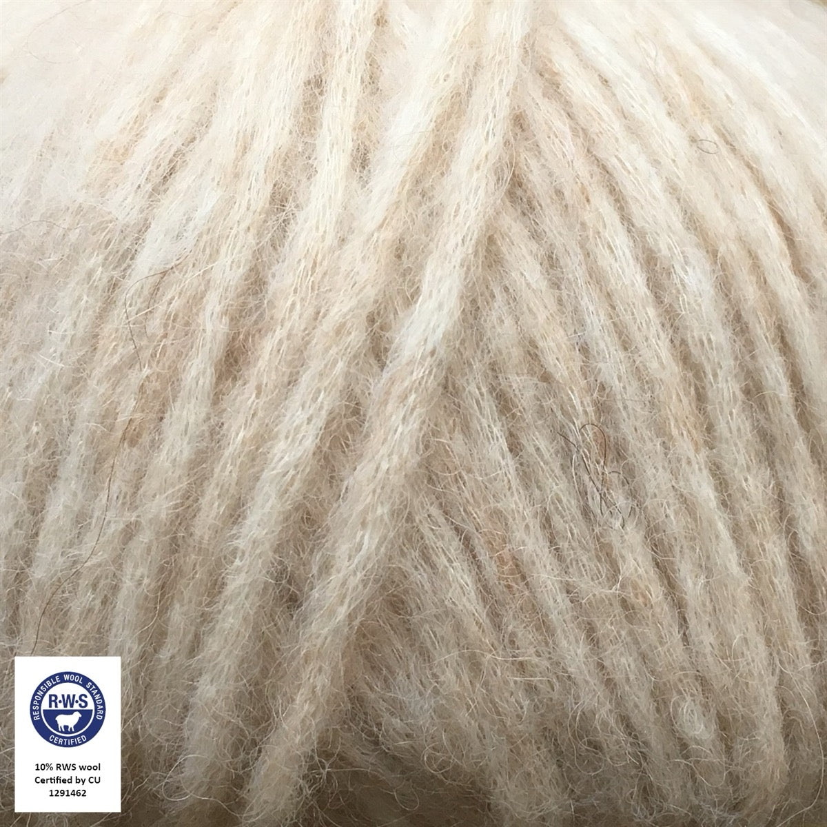 Close-up van een bol Snefnug-garen in een zachte, licht beige kleur. Dit lichte blowyarn heeft een kern van katoen met ingeblazen alpaca- en merinovezels, wat zorgt voor een luchtige, pluizige structuur. Onderaan zijn de RAS- en RWS-certificeringslogo's zichtbaar.