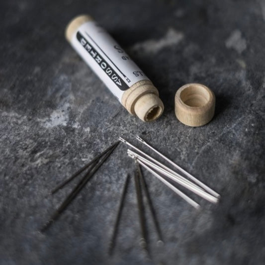 Close-up van een set Easy thread needles in verschillende diktes, uitgestald op een donker oppervlak, met een houten bewaarkoker op de achtergrond